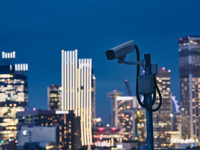 Security camera against illuminated urban skyline at night. Concept of surveillance, protection and safety.